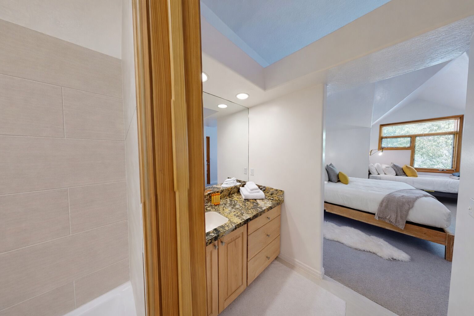 A modern bathroom with a granite countertop, wooden cabinets, and a large mirror.
