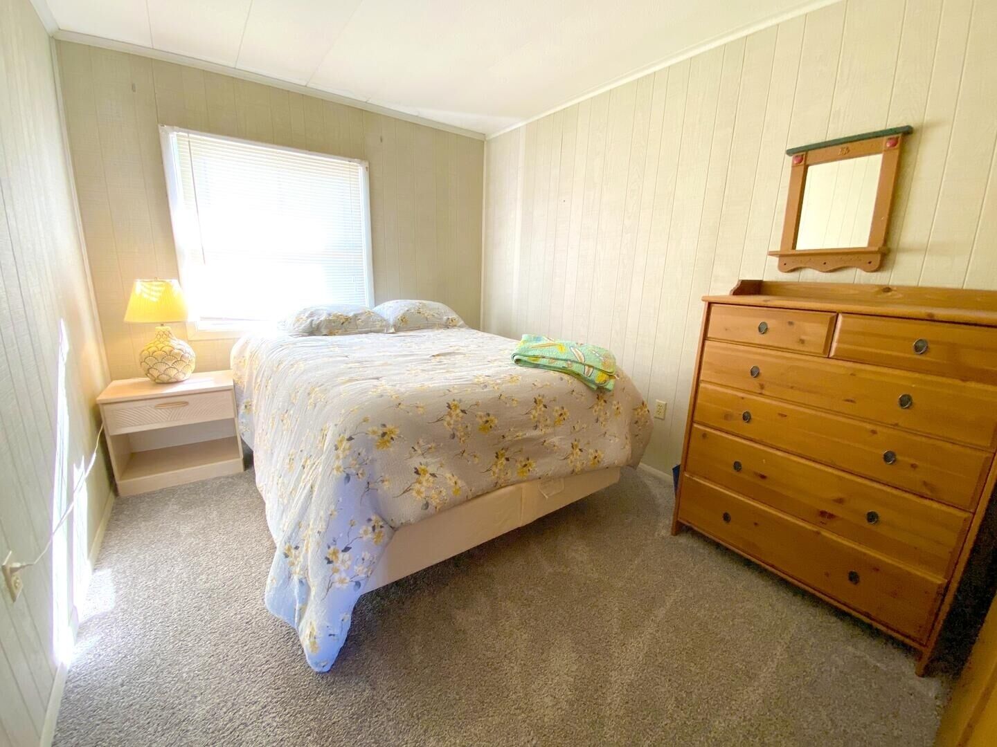 Ein Schlafzimmer mit Bett, Nachttisch mit Lampe, Kommode und Fenster mit Jalousien.