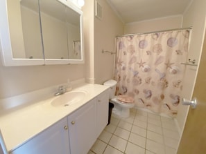 A bathroom with a white sink, a toilet, and a shower curtain with a seashell pattern. - Gullway Townhouse 2823 3 Bedroom Townhouse by RedAwning (Ocean City)