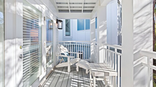 Une véranda couverte avec des balustrades blanches, un banc et une chaise avec des coussins.