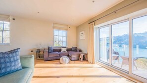 Relax in this serene space with a view of the water and distant hills, featuring a comfortable sofa and armchair.