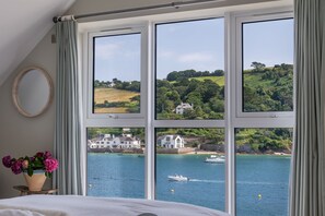 Enjoy a panoramic view of the coastal landscape from the comfort of this room, featuring a neatly made bed and a potted plant.