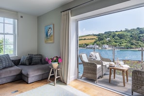 Relax in this stylish living room with a sofa, stool, and wicker chair, leading to an outdoor space with a scenic view.