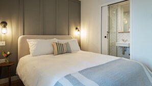 A neatly made bed with a striped blanket, a bedside table with a vase of flowers, and a modern bathroom with a glass shower enclosure. - Sea Cove -  an apartment that sleeps 4 guests in 2 bedrooms (Hope Cove)