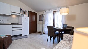 Een kleine keuken met een koelkast, fornuis en een eethoek met een tafel en stoelen.