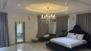 A modern bedroom with a large bed, a chandelier, and a view through a glass door. - Lovely nb 3-bed House in Opebi (Lagos)