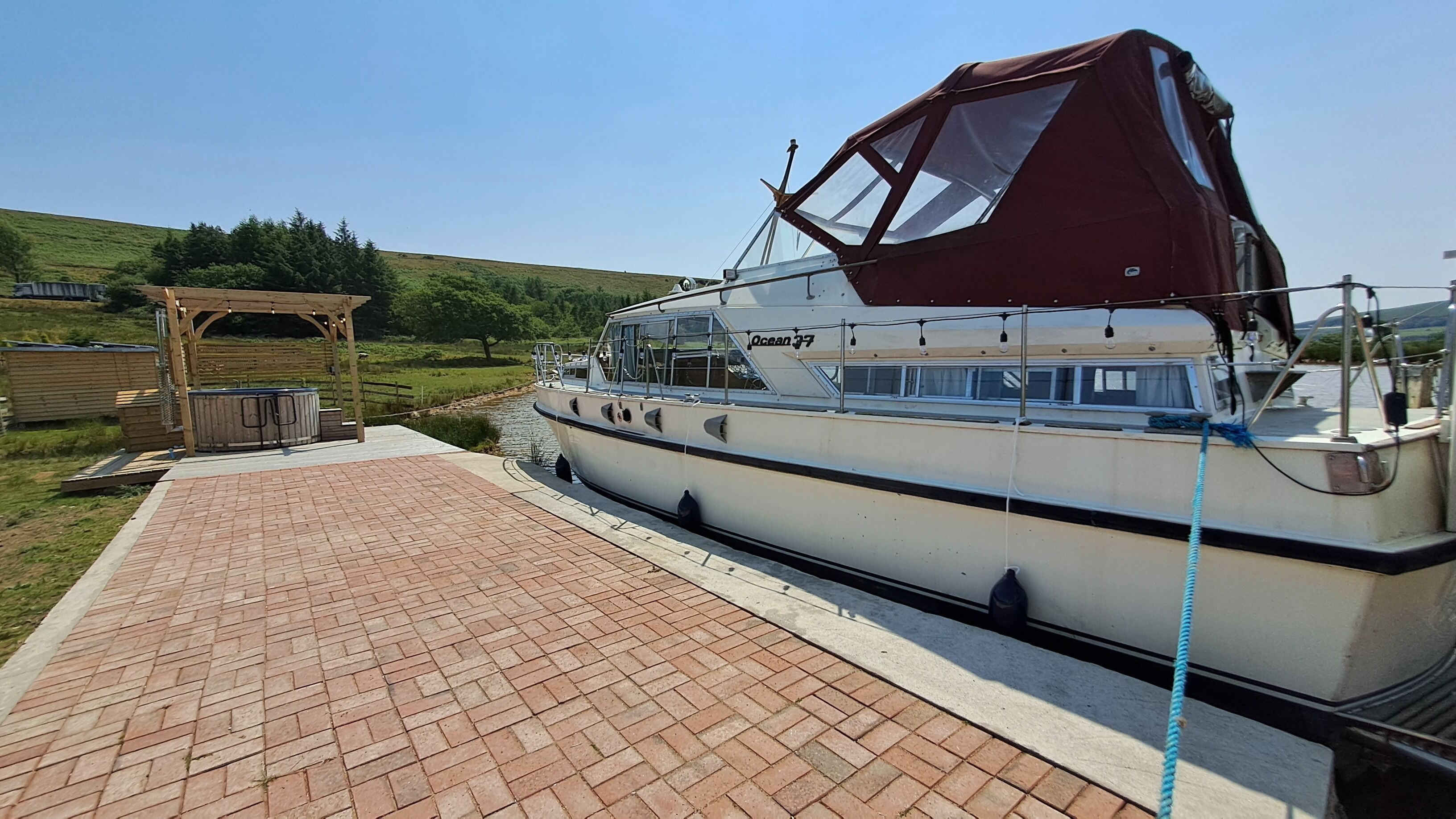 A boat docked at a pier with a covered deck and a wooden structure nearby.