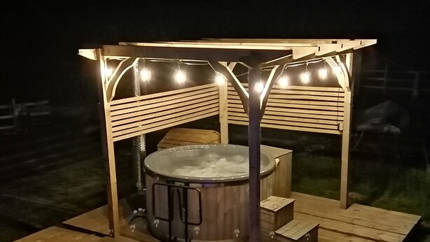 Ein Whirlpool unter einer Hollaube mit Lichterketten, umgeben von einer Holzterrasse.
