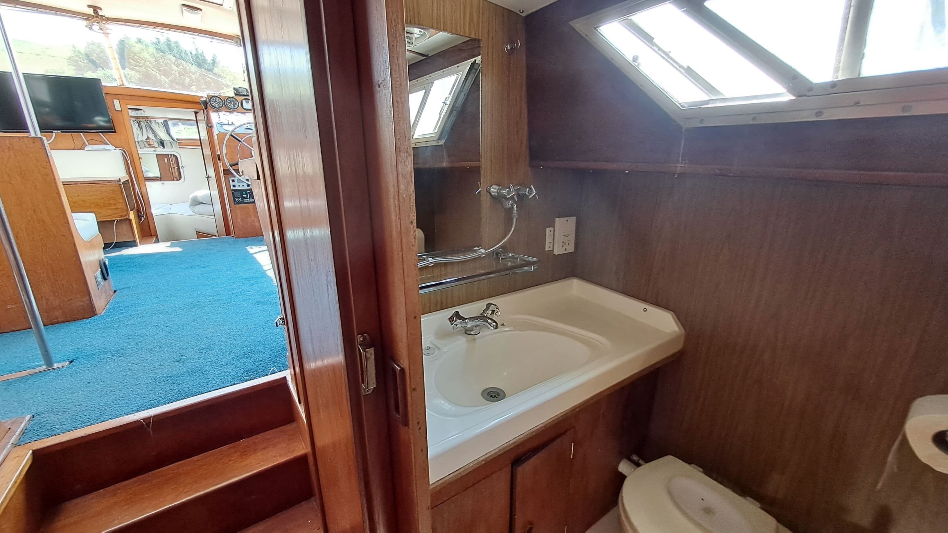 A compact bathroom with a sink, mirror, and toilet, featuring a skylight and wooden cabinetry.