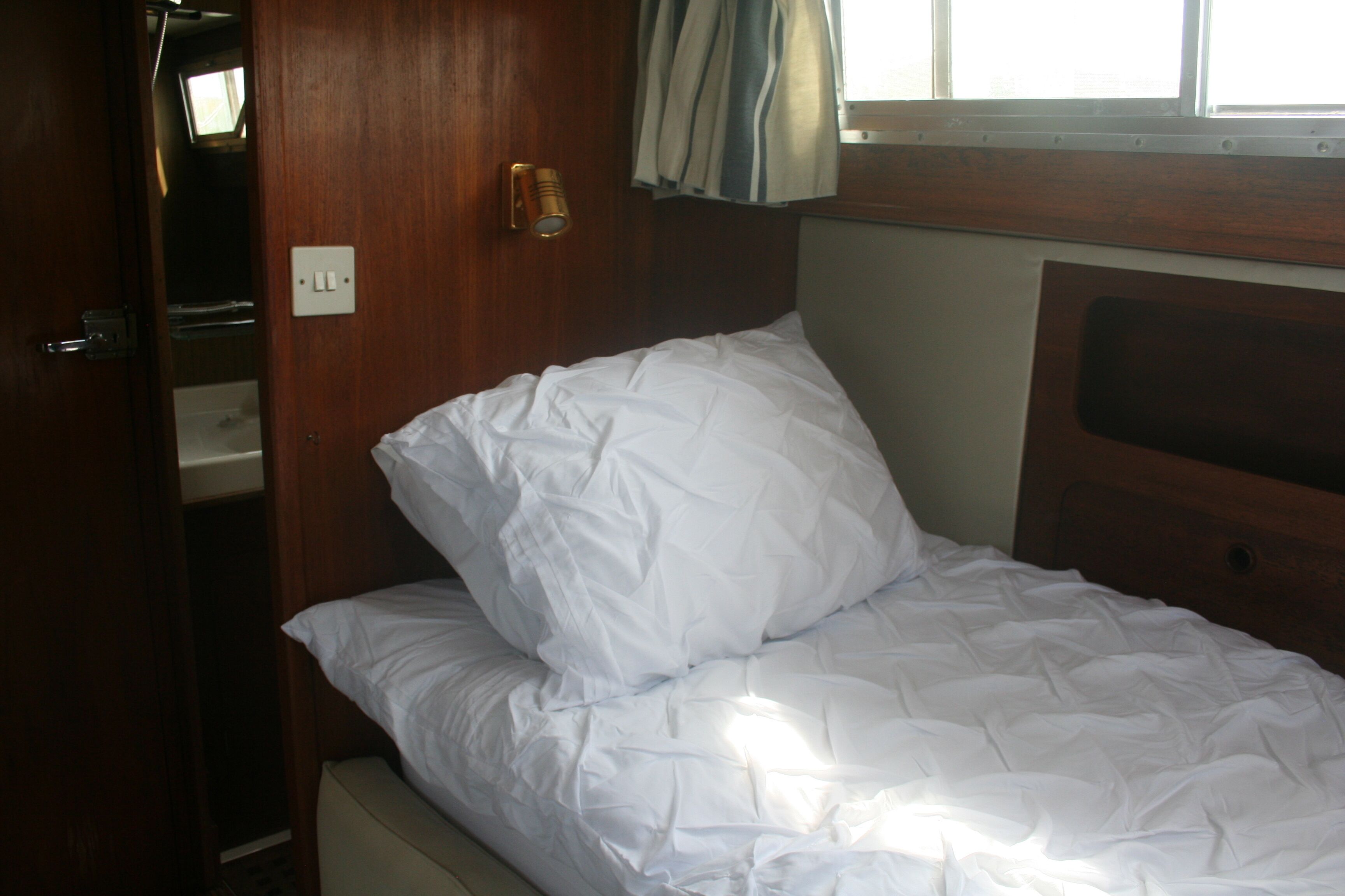 Una cama individual con ropa de cama blanca en una habitación con paredes de madera y una ventana con cortinas.