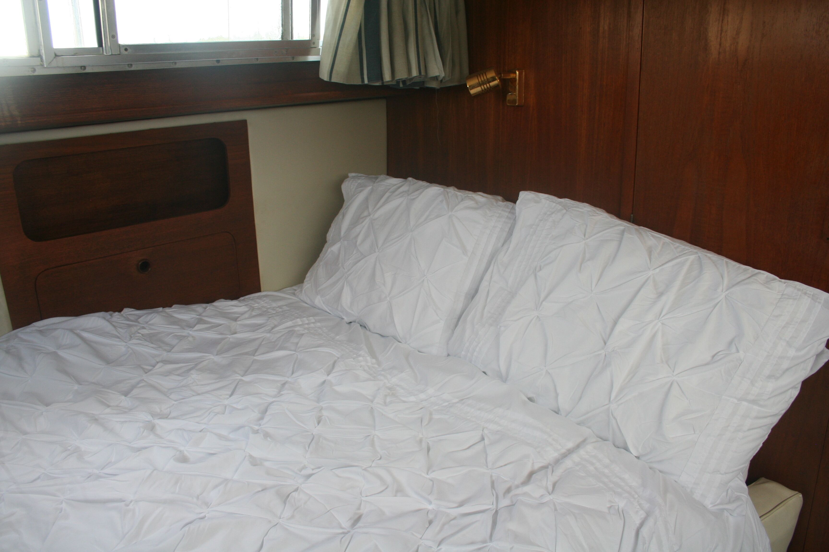 A bed with a wooden headboard, a window with curtains, and a wooden door with a brass handle.