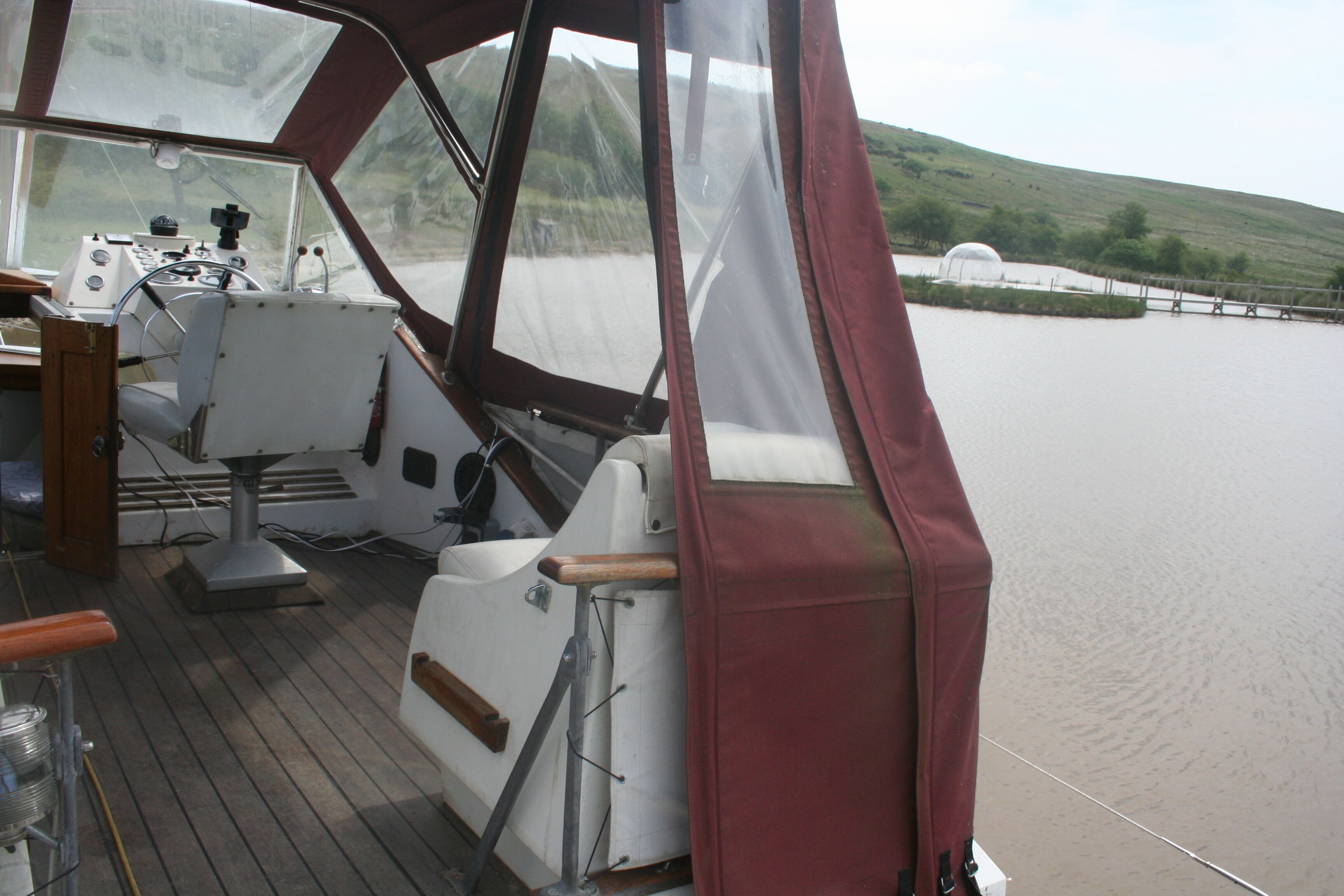 Interieur van een boot met een stuurwiel, bedieningspaneel en zitgedeelte.