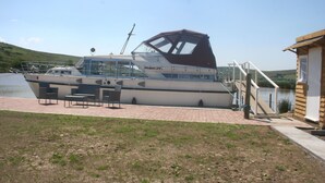 Ein Boot liegt in einer Marina festgemacht, mit einem überdachten Deck und einem kleinen Gebäude in der Nähe.