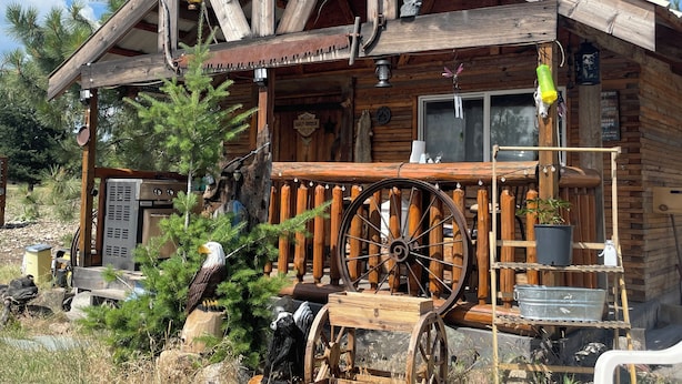 A rustic cabin with a porch, a large wooden wheel, and a sign indicating it is a motor home dealership. - Beautiful cabin with rustic charm in Eureka, MT! (Eureka)
