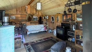 A rustic cabin interior with a wooden ceiling, a sofa, a television, a stove, and various kitchen items. - Beautiful cabin with rustic charm in Eureka, MT! (Eureka)