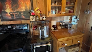 A compact kitchen with a stove, microwave, and a wooden cabinet above the counter. - Beautiful cabin with rustic charm in Eureka, MT! (Eureka)