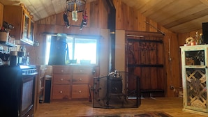 A rustic kitchen with wooden walls, a large window, and a hanging light fixture. - Beautiful cabin with rustic charm in Eureka, MT! (Eureka)