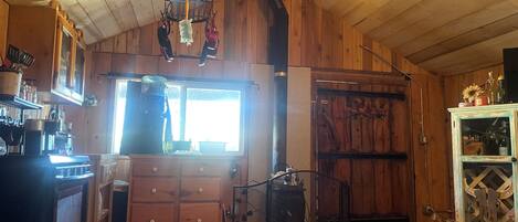 A rustic kitchen with wooden walls, a large window, and a hanging light fixture.