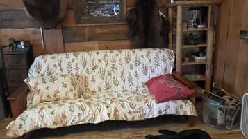 A room with a wooden wall, a sofa with floral upholstery, a black cat lying on the floor, and a mounted deer head.