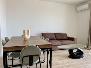 Ein modernes Wohnzimmer mit einem Holzes Esstisch, einem braunen Sofa und einem Glastisch.