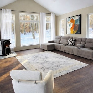 A living room with a sectional sofa, a fireplace, and large windows with a view of a snowy landscape.