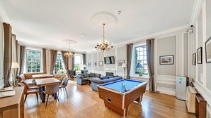 A spacious living room with a pool table, a dining area with a wooden table and chairs, a sofa, and a television. - Hambleton Hall Apt (Thirsk)
