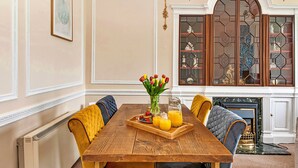 A dining area with a wooden table, yellow and blue upholstered chairs, a tray with fruit and juice, and a vase of tulips. - Hambleton Hall Apt (Thirsk)