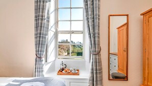 A bedroom with a large window, a bedside table with a tray of breakfast, a bed with a blanket, and a wardrobe.