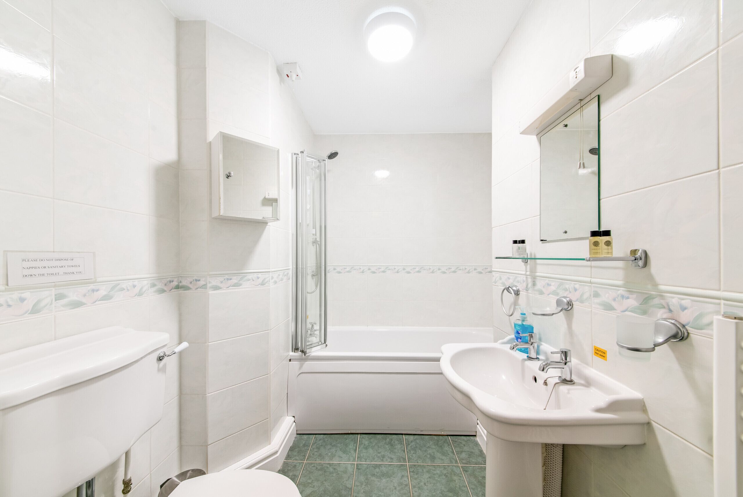 A bathroom with a toilet, sink, shower, and a glass-enclosed shower stall.