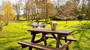 A picnic table with a metal container in the center, surrounded by a grassy area with trees and a small waterfall in the background. - Pennine Hall Apt (Thirsk)