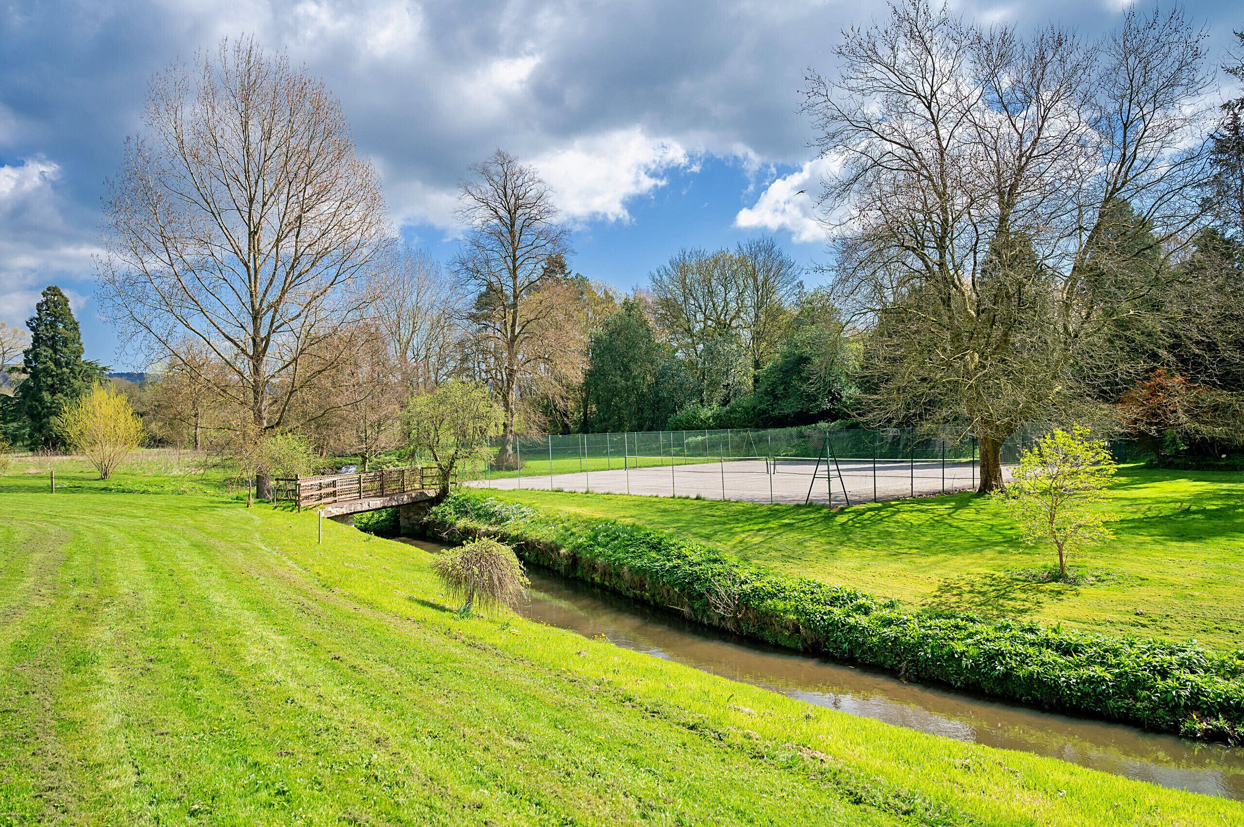Ein Park mit einer Rasenfläche, einem kleinen Bach und einer Brücke.