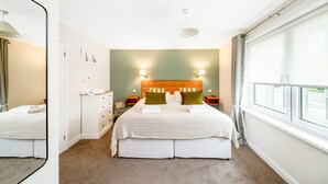 A hotel room with a large bed, a wooden headboard, two bedside tables, a mirror, and a window with curtains. - Ryedale Hall Cottage (Thirsk)