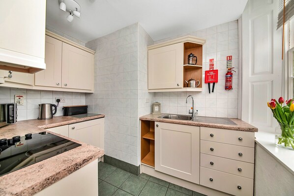 A modern kitchen with beige cabinets, a built-in stove, a sink, and a small wooden shelf.