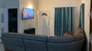 Ein Wohnzimmer mit einer Couch, einem an der Wand befestigten Fernseher, einer Tür und einem Vorhang.
