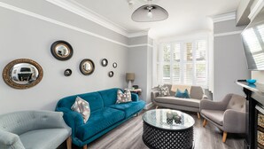 A living room with a teal sofa, a grey armchair, a round coffee table, and a fireplace. - 7 Longfield Terrace · Gorgeous Central 5 Bed House in York with Parking - Pass The Keys (York)