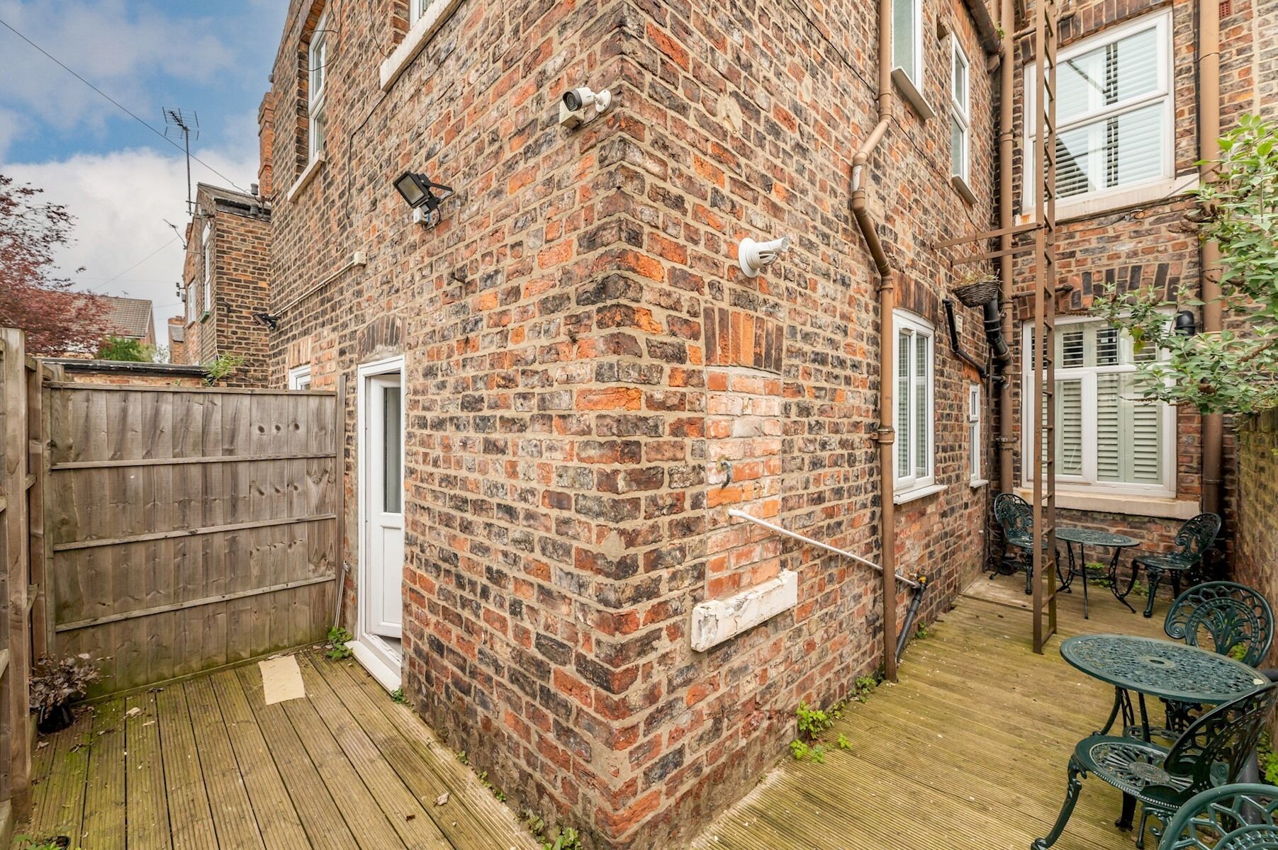 Ein Backsteinhaus mit einer Holzdachterrasse, Sitzmöglichkeiten im Freien und einer weißen Tür.