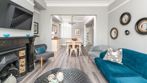 A modern living room with a fireplace, a TV, a dining area, and a blue sofa. - 7 Longfield Terrace · Gorgeous Central 5 Bed House in York with Parking - Pass The Keys (York)