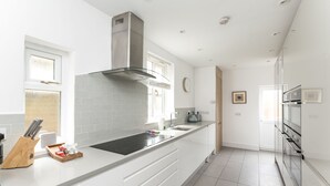 A modern kitchen with white cabinetry, a stainless steel range hood, a built-in oven, and a large window providing natural light. - 7 Longfield Terrace · Gorgeous Central 5 Bed House in York with Parking - Pass The Keys (York)
