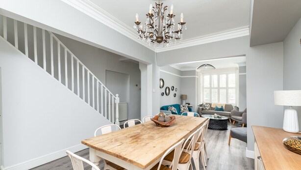 A spacious living area with a wooden dining table, white chairs, a blue sofa, and a chandelier. - 7 Longfield Terrace · Gorgeous Central 5 Bed House in York with Parking - Pass The Keys (York)