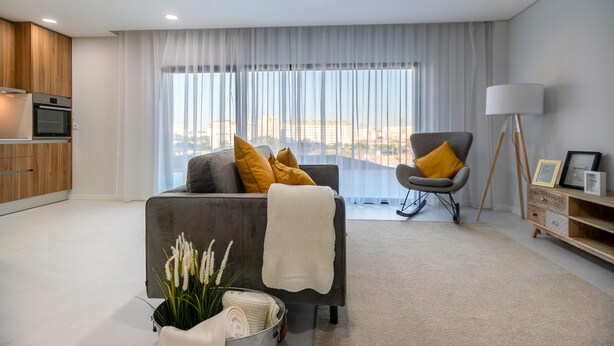 Un salon moderne avec un canapé gris, un fauteuil à bascule, un coin repas doté de meubles en bois et une grande fenêtre offrant une vue sur la ville.