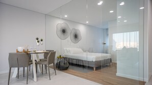 Une chambre moderne avec une cloison en verre, un lit, une table de chevet et un coin repas avec des chaises et une table.