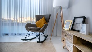 Un salon moderne avec un fauteuil à bascule, une lampe sur pied et un meuble en bois orné de cadres photos.