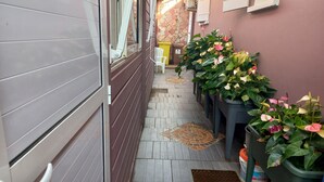 A narrow hallway with a tiled floor, a door on the left, and potted plants on the right.