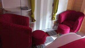 A room with two red armchairs, a small ottoman, a white sofa, and a television mounted on the wall.