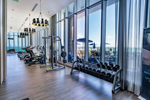 A modern gym with exercise equipment, large windows, and a view of the ocean.