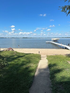 A beach with a concrete path leading to a dock extending into a calm lake. - Beach Home on Storm Lake (Lakeside)