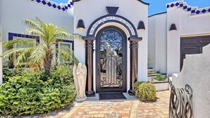 Un ingresso di un edificio con un cancello decorativo, una statua e un giardino curato.
