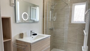 A modern bathroom with a glass-enclosed shower, a large mirror, and a white sink. - Maison de Village, 3 Chambres, Fibre (Dunes)