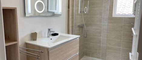 A modern bathroom with a glass-enclosed shower, a large mirror, and a white sink.