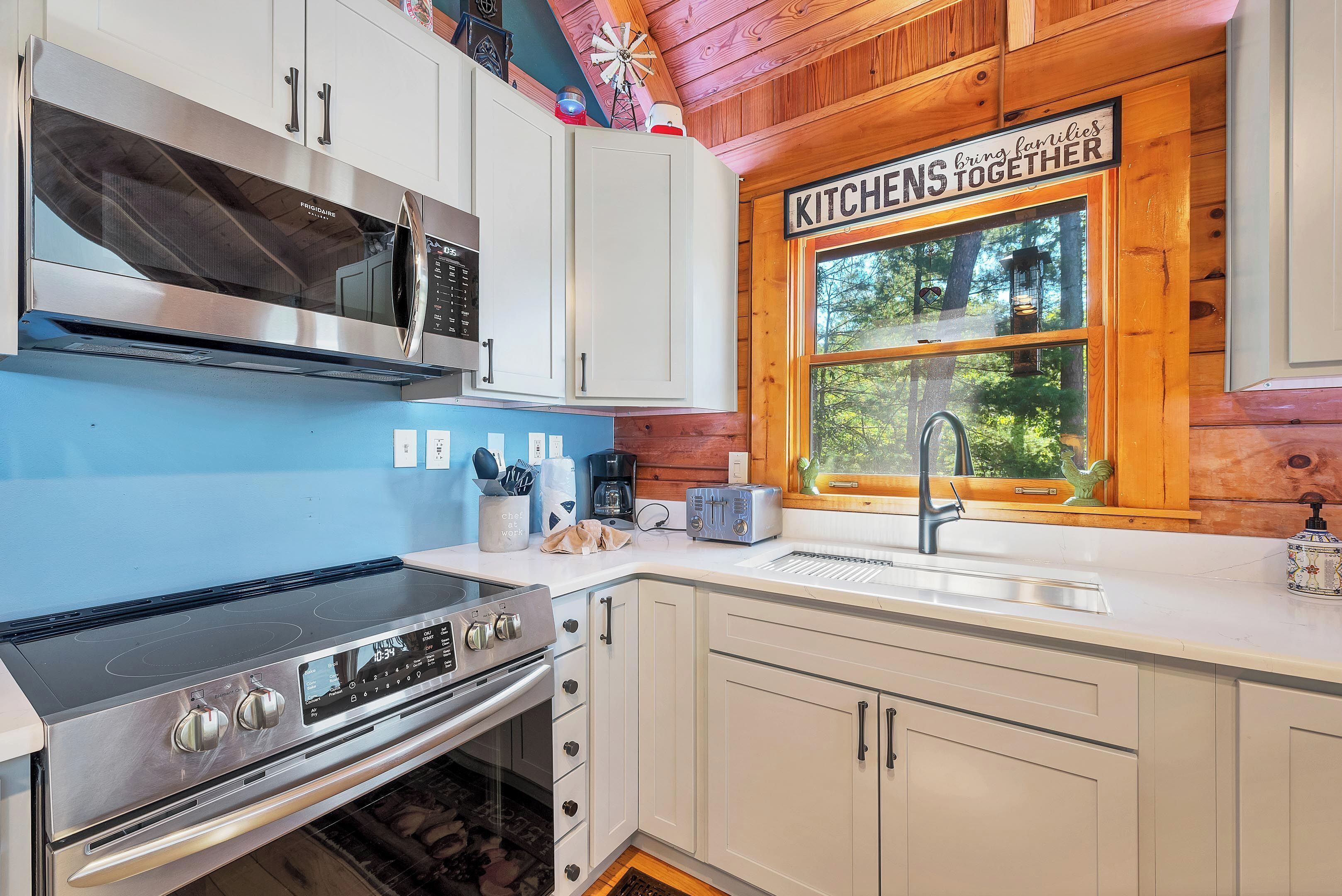 A modern kitchen with stainless steel appliances, white cabinetry, and a window with a view of greenery.